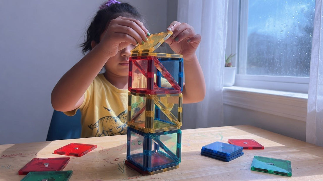 Kind van negen jaar bouwt een hoge toren van gekleurde magnetische tegels aan een tafel bij het raam